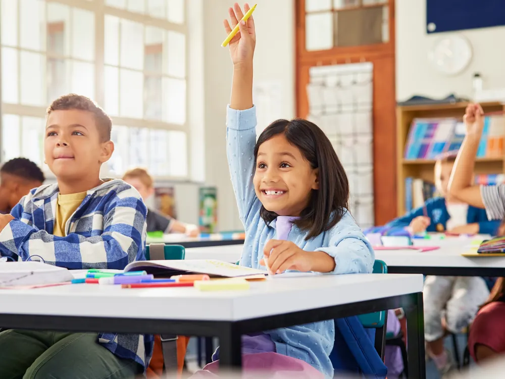 Primary school students in class, one with her hand raised